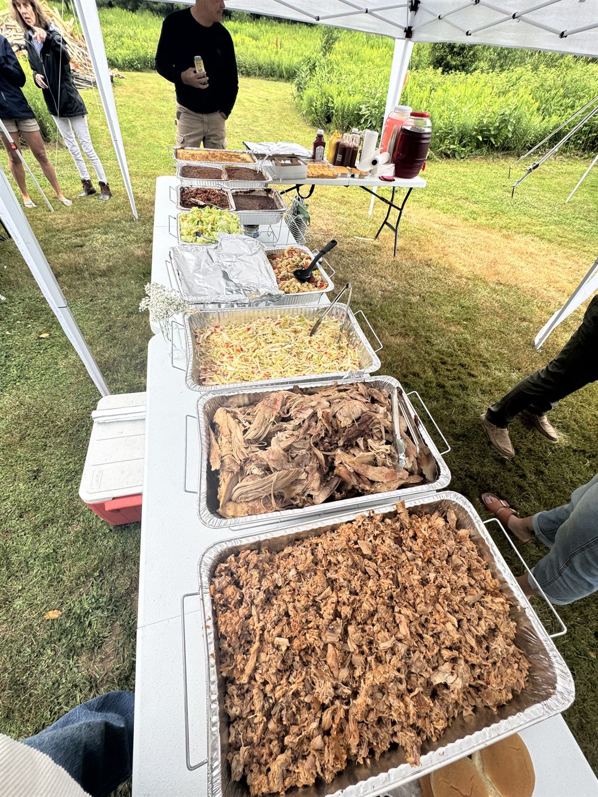 Foil trays of pulled pork and sides lined up on the serving table